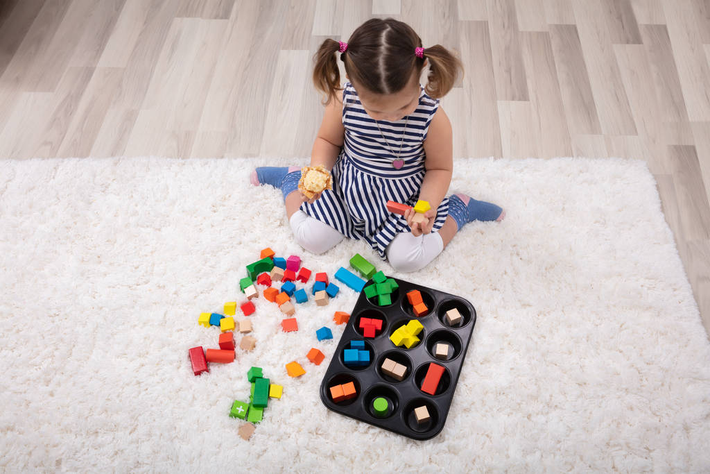 Verhoogde weergave van meisje zittend op tapijt spelen met kleurrijke blokken thuis - Foto, afbeelding