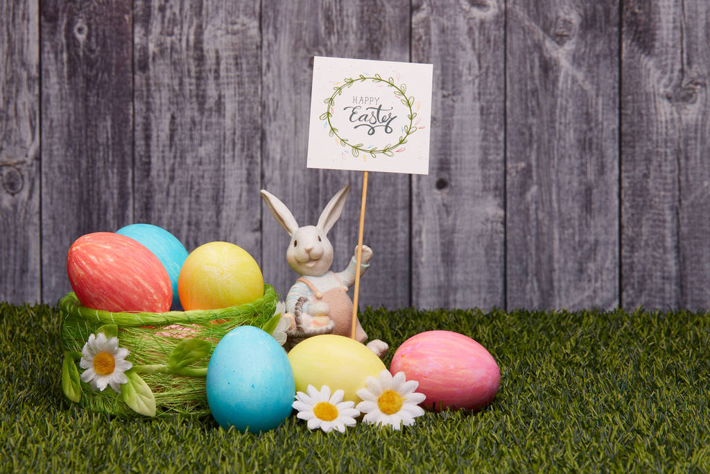 Χρωματιστά πασχαλινά αυγά, πασχαλινό κουνέλι και λουλούδια ξαπλωμένα σε πράσινο γρασίδι σε γκρι ξύλινο φόντο με χώρο αντιγραφής. Ευχετήρια κάρτα, φόντο του Πάσχα - Φωτογραφία, εικόνα