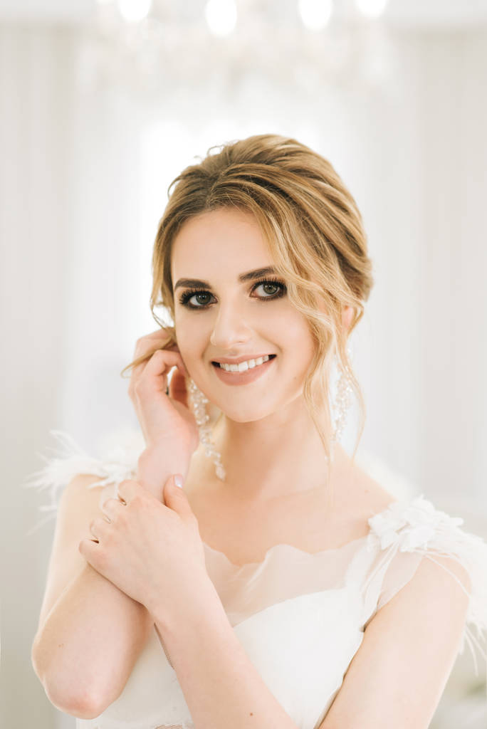 Portrait of a beautiful young bride in a bright room in a romantic atmosphere. Bride in a negligee with wedding hair and makeup - Photo, Image