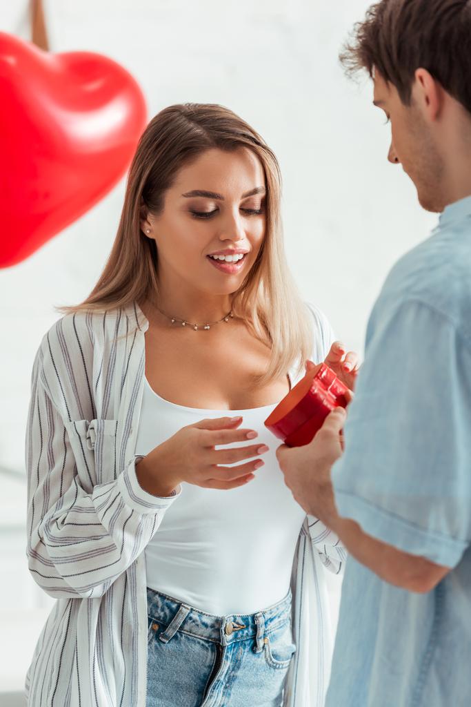 Mann hält herzförmige Geschenkschachtel in der Nähe der schönen Freundin am Valentinstag  - Foto, Bild
