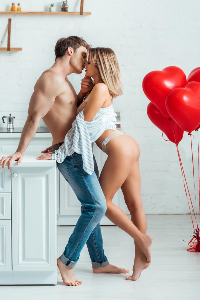 Heißes Paar küsst sich in der Nähe roter herzförmiger Ballons  - Foto, Bild