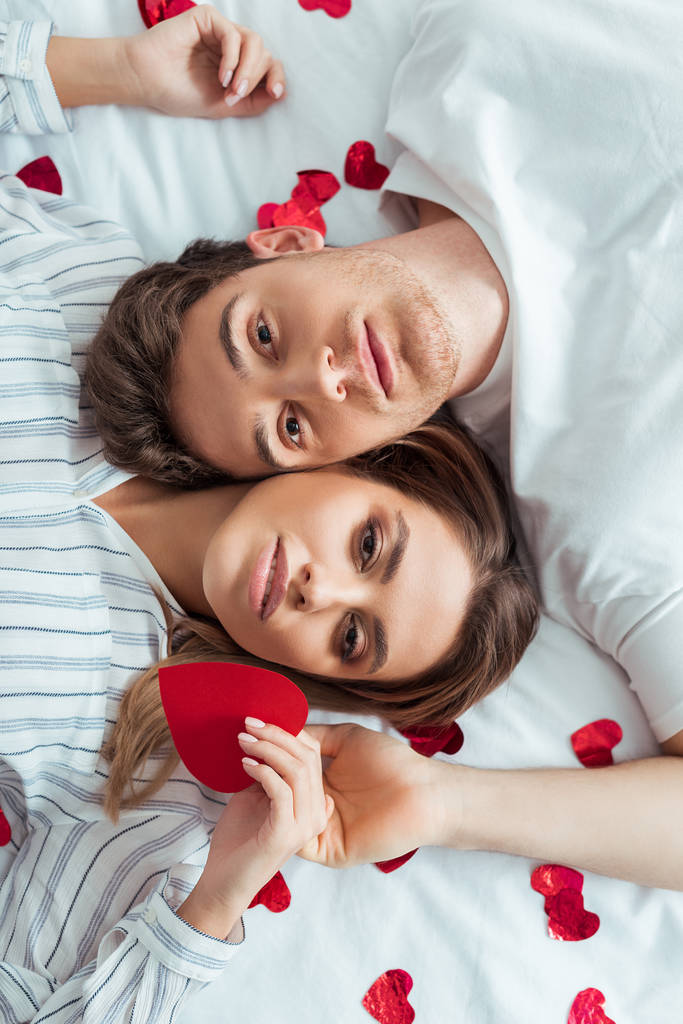 top kilátás jóképű férfi és vonzó nő feküdt az ágyon közelében piros szív  - Fotó, kép