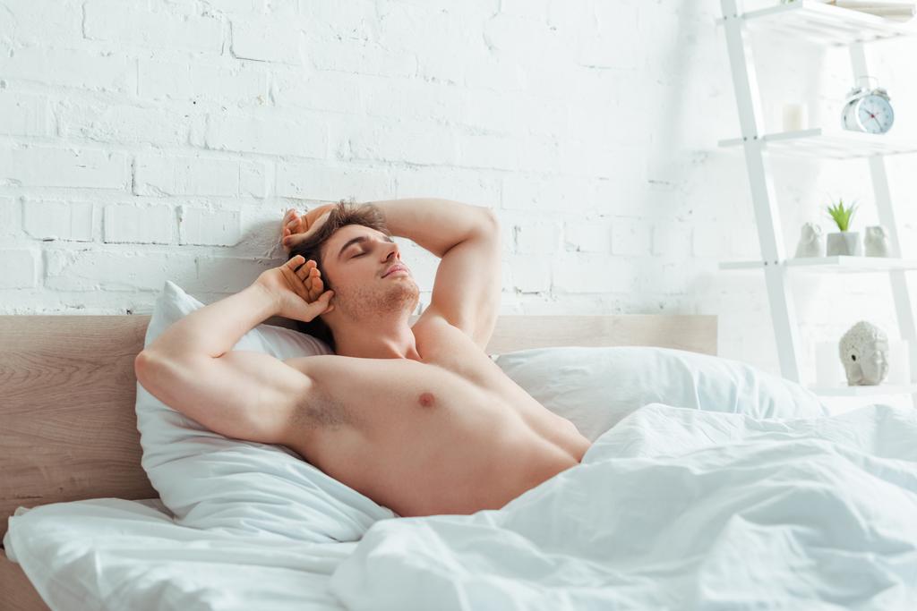 μυώδης άνδρας με κλειστά μάτια ξαπλωμένος στο κρεβάτι  - Φωτογραφία, εικόνα