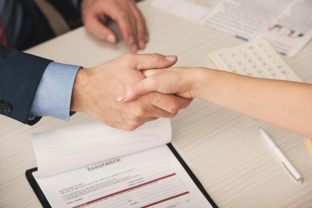 cropped view of agent and client shaking hands near clipboard with insurance lettering  - Photo, Image