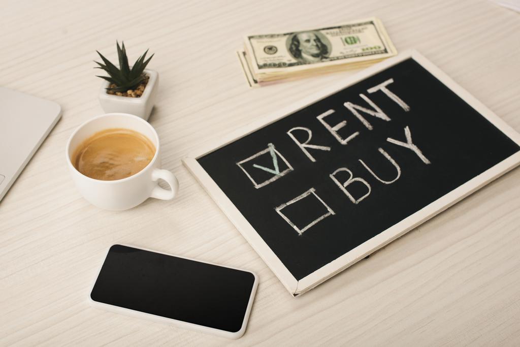 chalkboard with rent and buy lettering near cup of coffee, plant, smartphone with blank screen and money  - Photo, Image