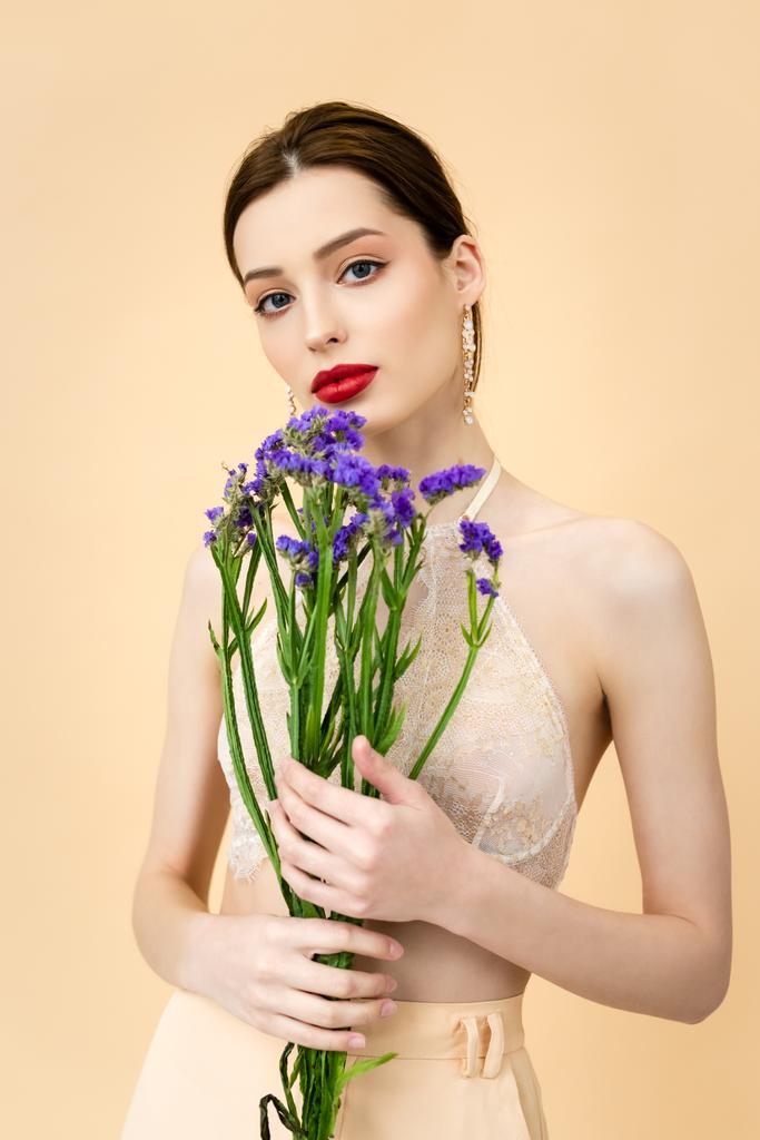 donna attraente che tiene fiori di limonio viola isolati sul beige
  - Foto, immagini