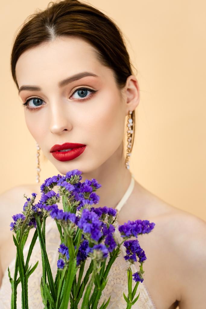 piękna kobieta patrząc na aparat w pobliżu fioletowy limonium kwiaty izolowane na beżu  - Zdjęcie, obraz