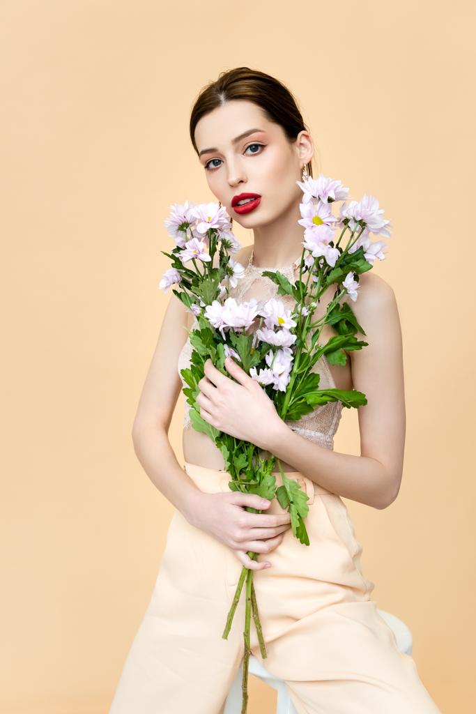 beautiful woman with red lips holding blooming flowers isolated on beige  - 写真・画像
