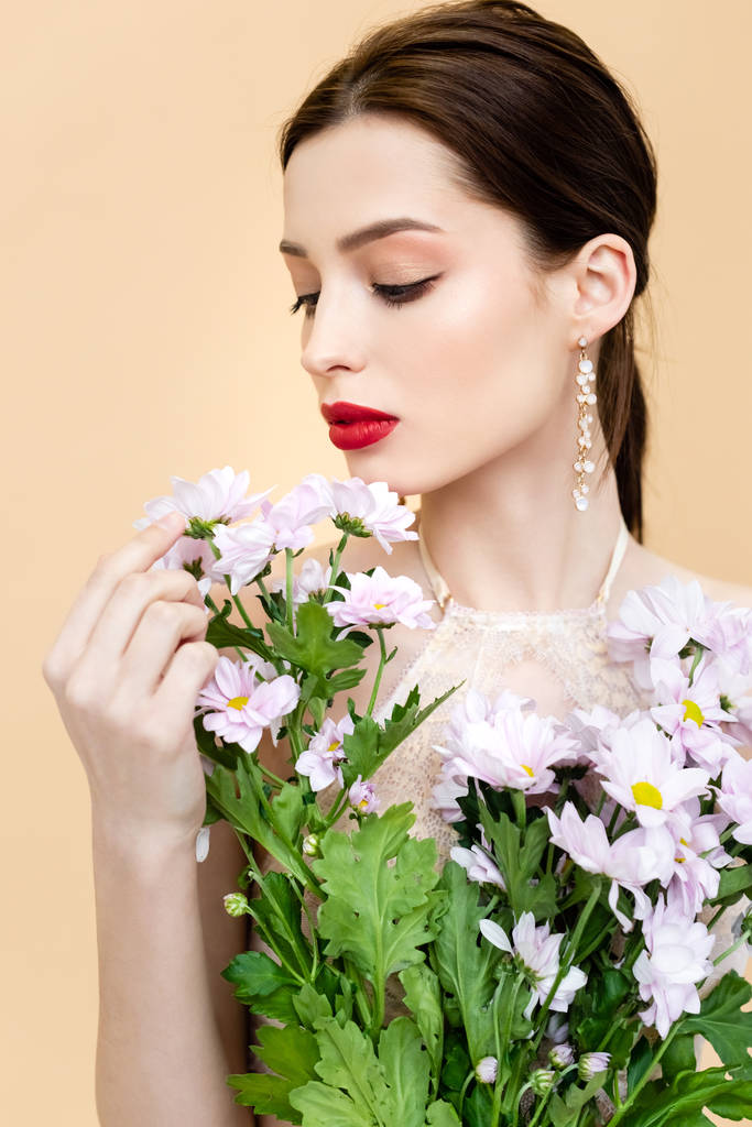 giovane donna guardando fiori di crisantemo in fiore isolati su beige
  - Foto, immagini