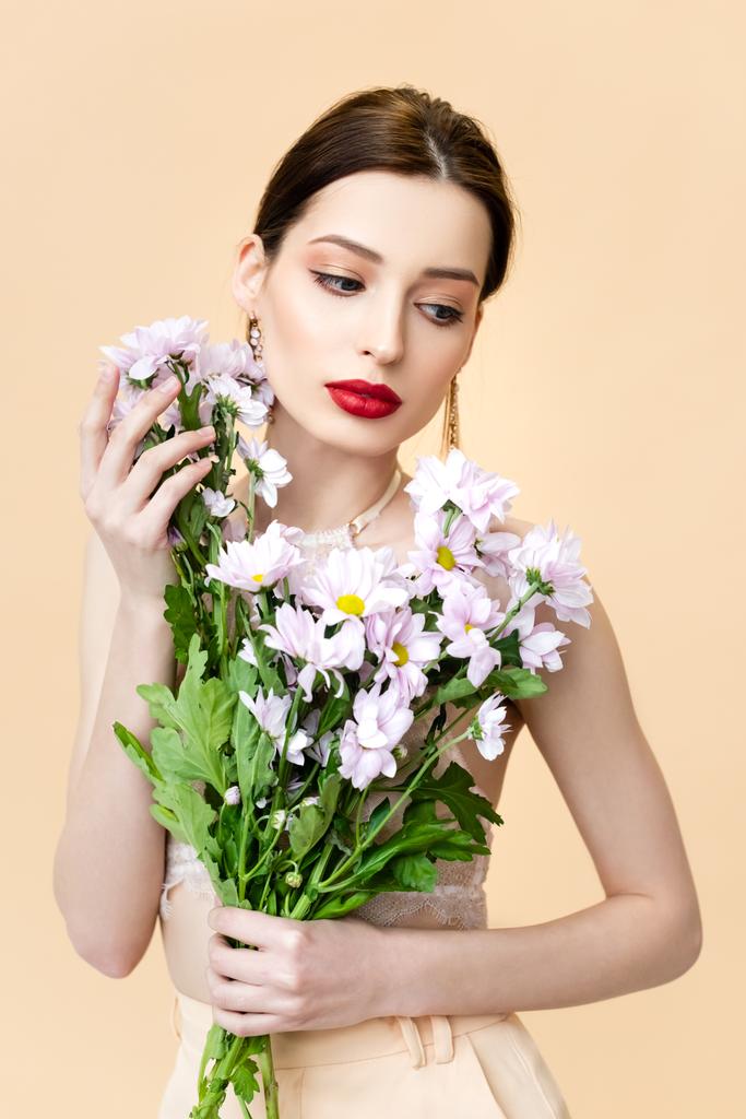 pretty young woman looking away near blooming chrysanthemum flowers isolated on beige  - Photo, Image