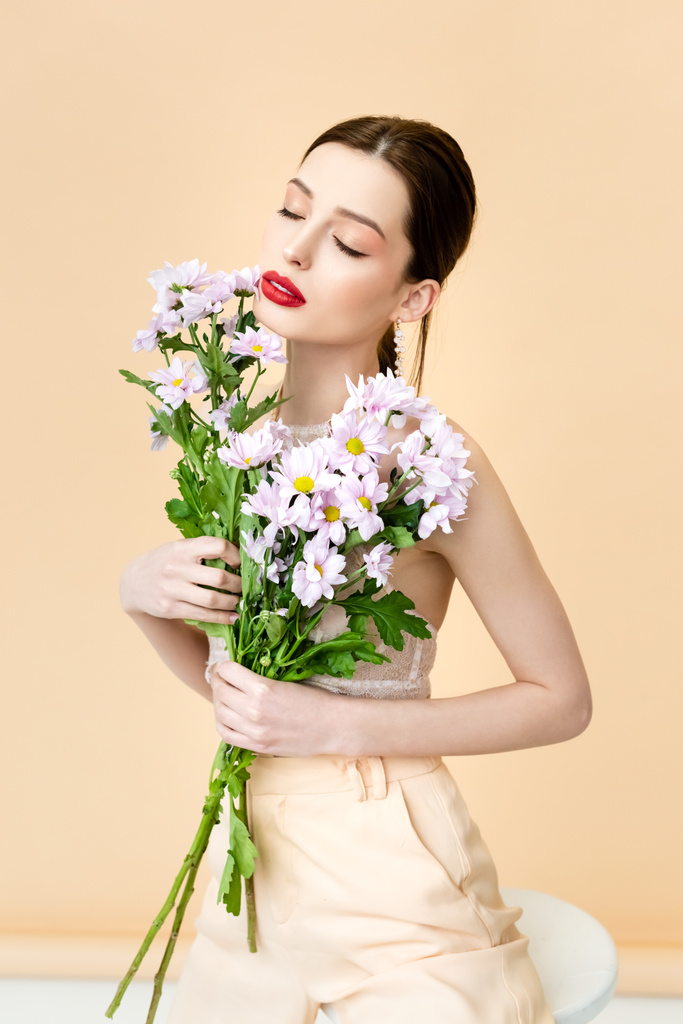 гарна жінка з закритими очима тримає квітучі квіти хризантем на бежевому
  - Фото, зображення