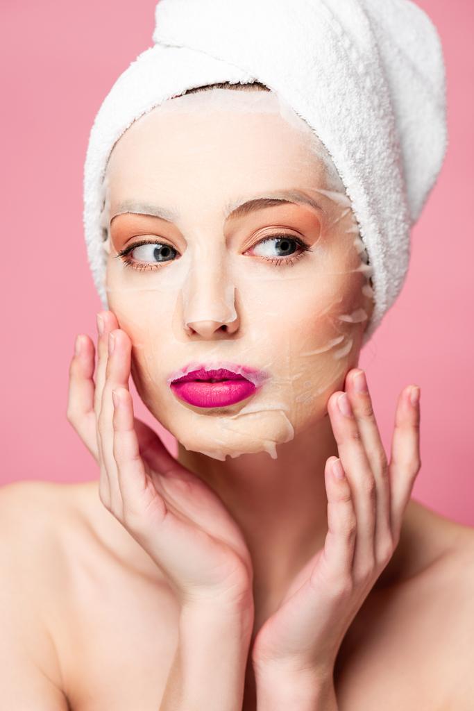 mladá nahá žena v hydratační obličejové masky při pohledu pryč izolované na růžové  - Fotografie, Obrázek