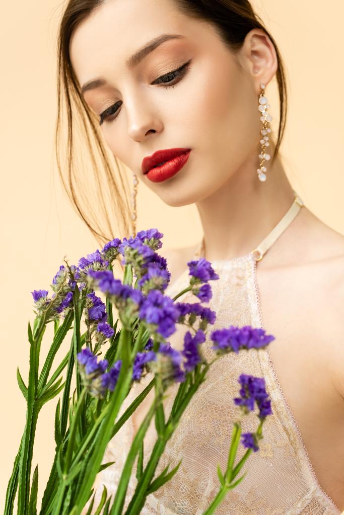 mladá a atraktivní žena drží fialové limonium květiny izolované na béžové  - Fotografie, Obrázek