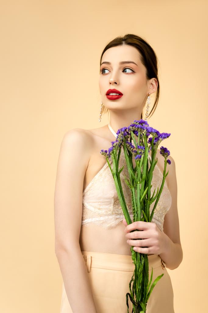jovem mulher atraente segurando flores de limonium e olhando para longe isolado no bege
  - Foto, Imagem