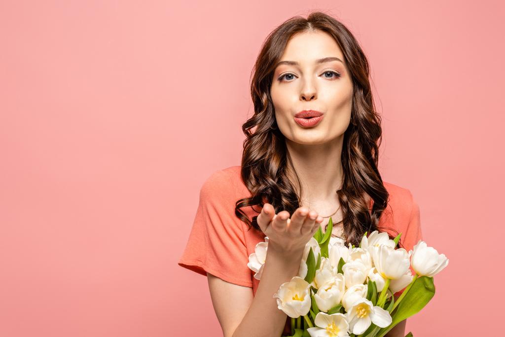 attractive girl blowing air kiss at camera while holding bouquet of white tulips isolated on pink - Photo, Image