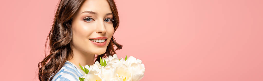panoramic shot of happy girl holding bouquet of white tulips and looking at camera isolated on pink - Photo, Image