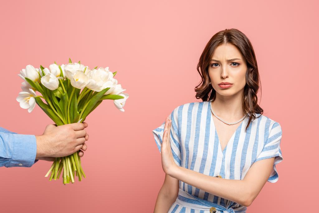 gedeeltelijke weergave van de man presenteren boeket van witte tulpen ontevreden meisje toont geen gebaar geïsoleerd op roze - Foto, afbeelding
