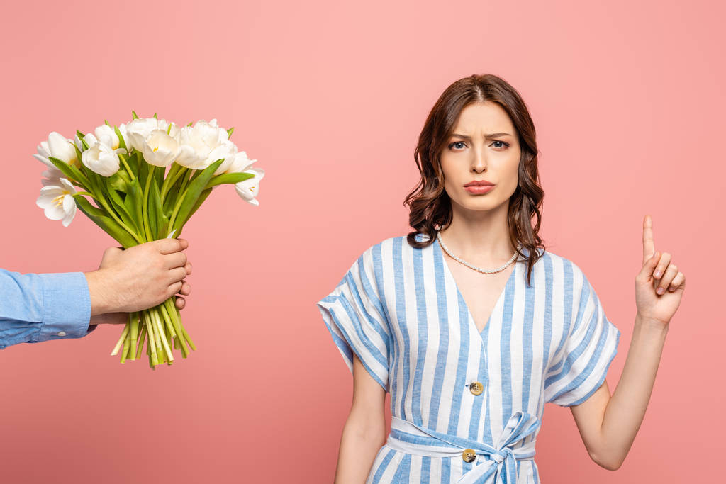 vista parziale dell'uomo che presenta bouquet di tulipani bianchi a ragazza seria mostrando idea gesto isolato su rosa
 - Foto, immagini