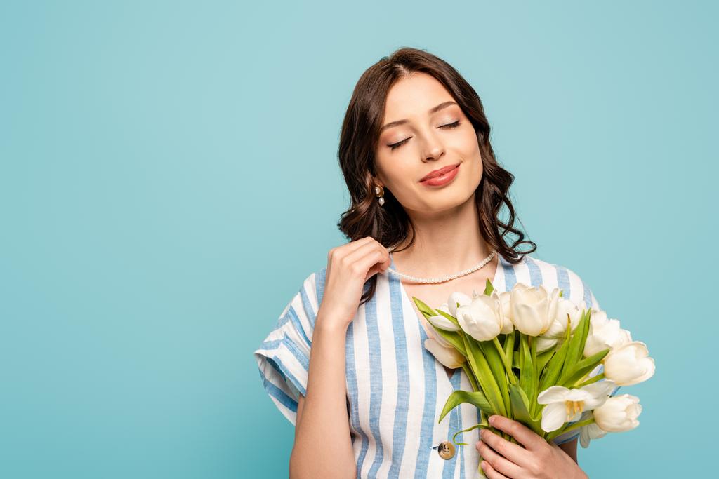 szczęśliwa kobieta trzyma bukiet białych tulipanów i uśmiecha się z zamkniętymi oczami odizolowane na niebiesko - Zdjęcie, obraz
