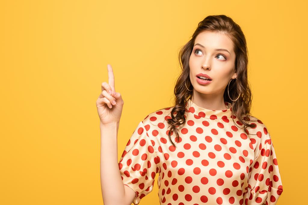thoughtful young woman looking up while showing idea gesture isolated on yellow - Photo, Image