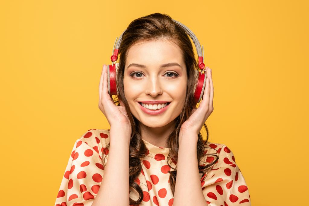 jeune femme heureuse touchant écouteurs tout en souriant à la caméra isolée sur jaune
 - Photo, image