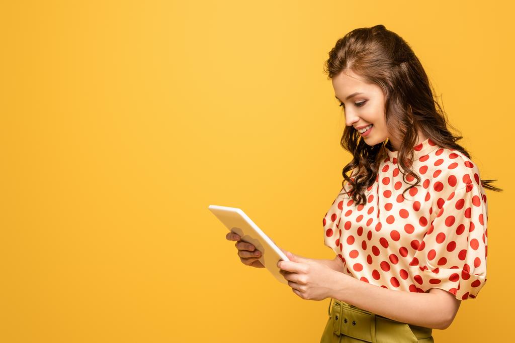 νεαρή γυναίκα χαμογελώντας κατά τη χρήση ψηφιακή ταμπλέτα απομονώνονται σε κίτρινο - Φωτογραφία, εικόνα