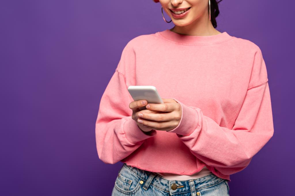 abgeschnittene Ansicht eines lächelnden Mädchens im Chat auf dem Smartphone isoliert auf lila - Foto, Bild