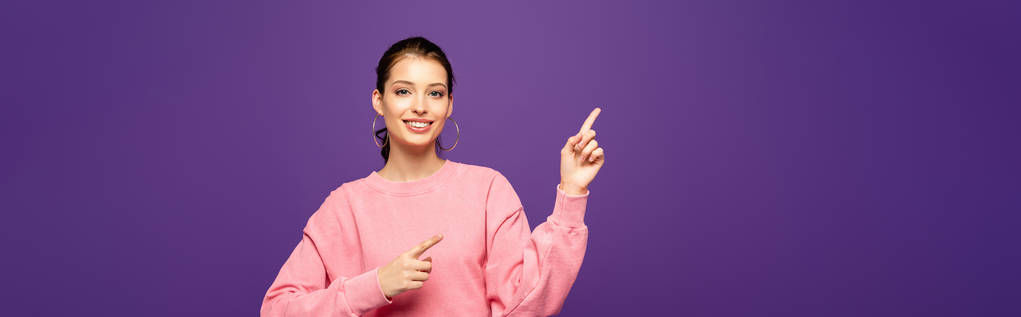 панорамный снимок веселой девушки, улыбающейся в камеру, указывая пальцами, изолированными на фиолетовый
 - Фото, изображение
