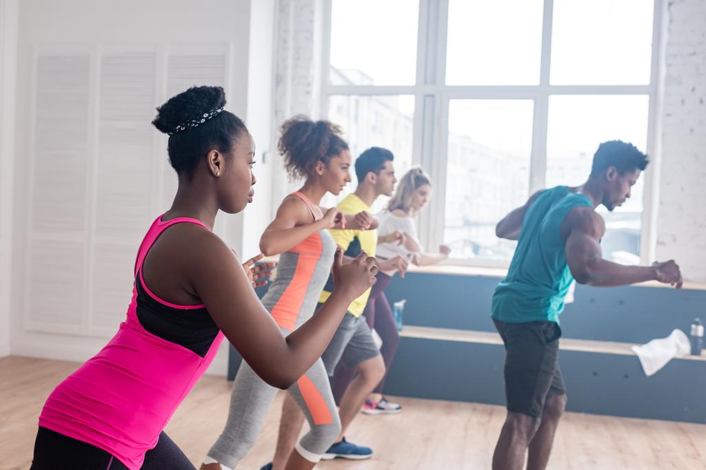 Vista lateral de dançarinos multiculturais aprendendo movimentos de zumba com treinador afro-americano em estúdio de dança
 - Foto, Imagem