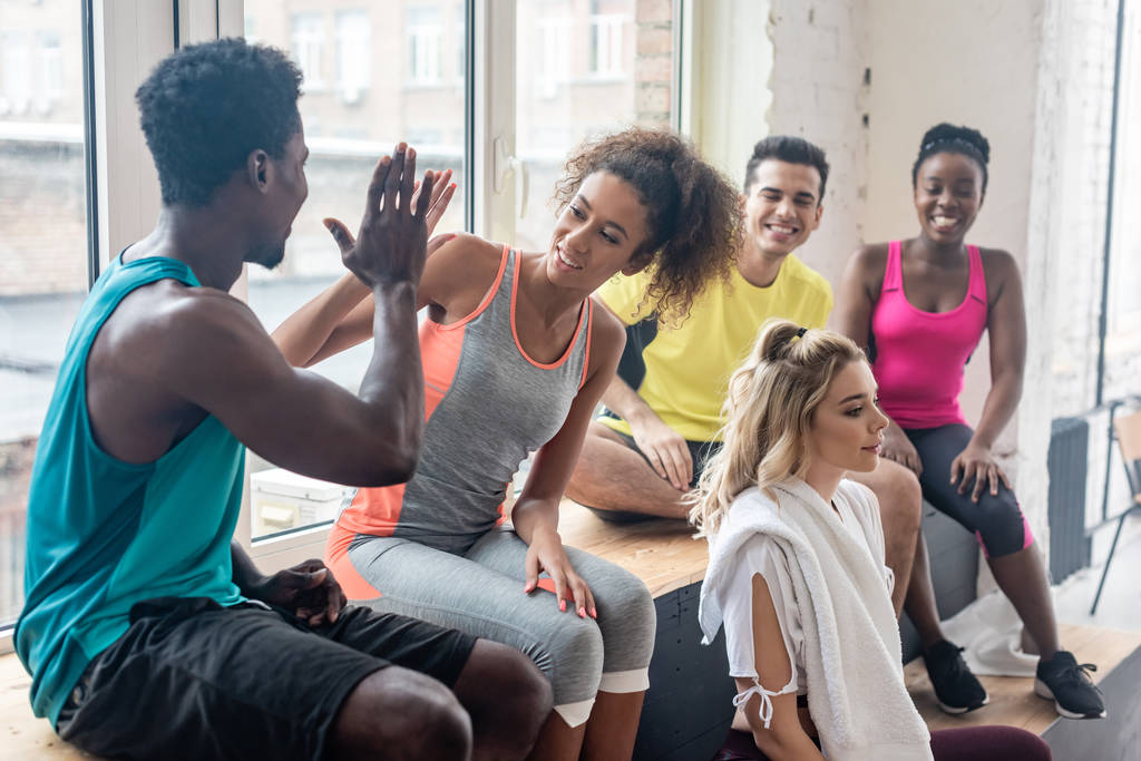 Enfoque selectivo de sonrientes bailarines afroamericanos zumba high five mientras descansan en estudio de danza
 - Foto, imagen