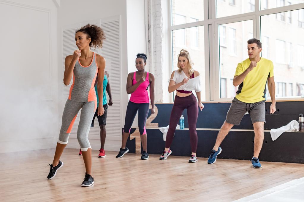 Beautiful african american trainer performing zumba movements with multicultural dancers in dance studio with smoke - Photo, Image