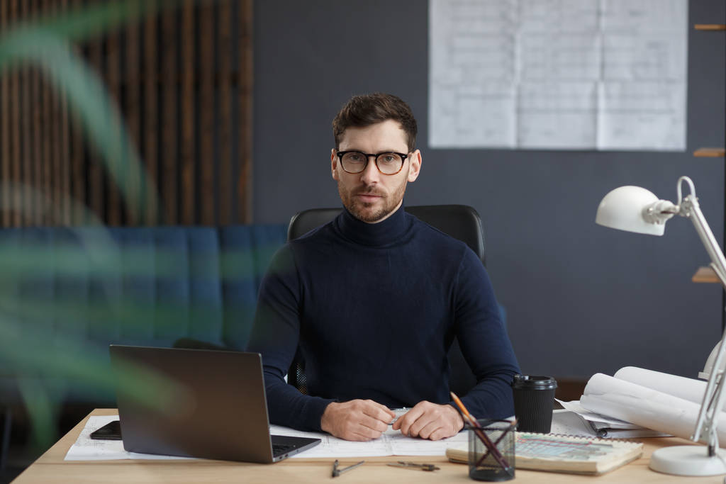 Arquitecto trabajando en oficina con laptop. Retrato de negocios de un hombre barbudo guapo con anteojos sentados en el trabajo. Un hombre de negocios seguro tuvo éxito. Concepto empresarial - Foto, Imagen
