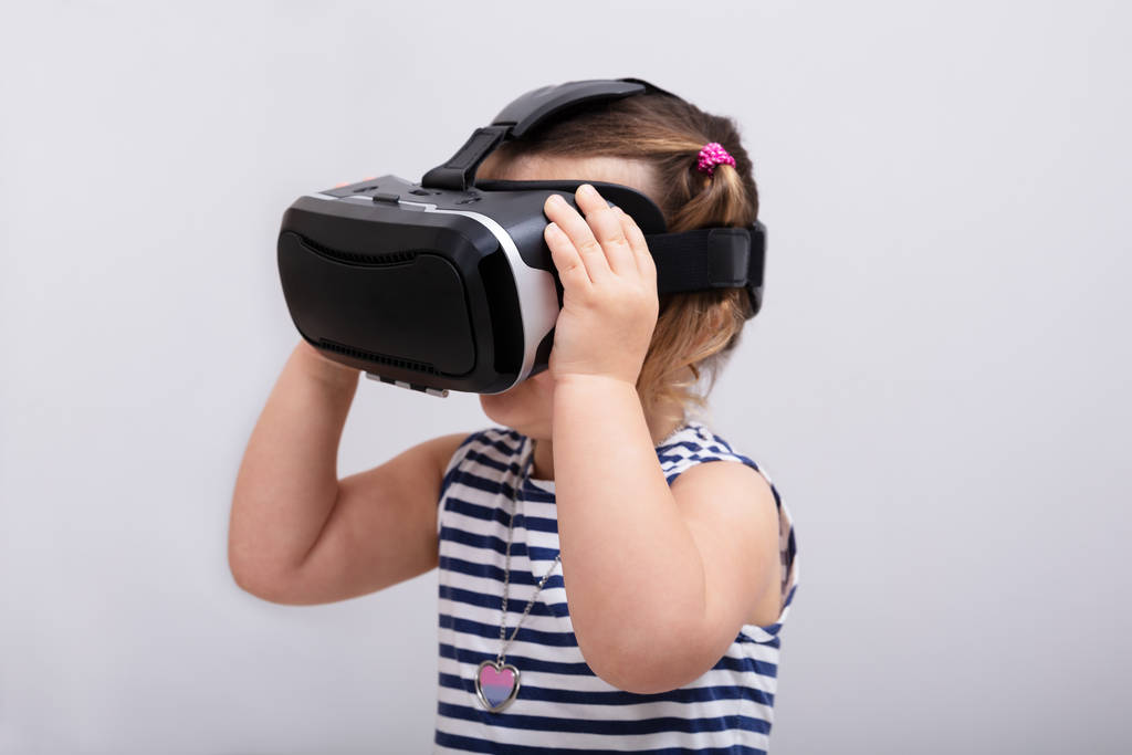Маленькая девочка с помощью гарнитуры виртуальной реальности на белом фоне
 - Фото, изображение