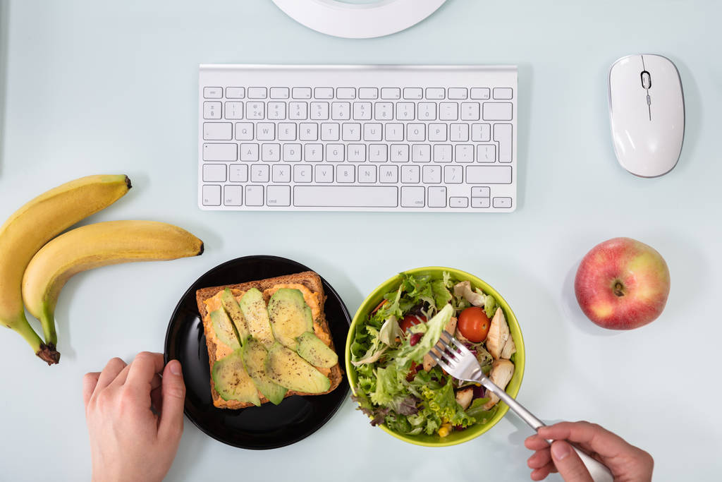 Een overhead zicht op de hand van ondernemer salade met vork op het Bureau - Foto, afbeelding