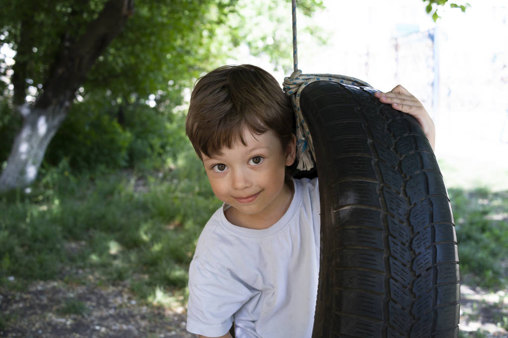 Happy Boy jugando en una rueda basculante en el jardín. Soleado verano d
 - Foto, imagen