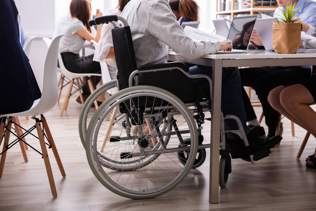 Vista lateral de un hombre de negocios discapacitado sentado en una silla de ruedas usando el ordenador portátil trabajando en la oficina
 - Foto, Imagen