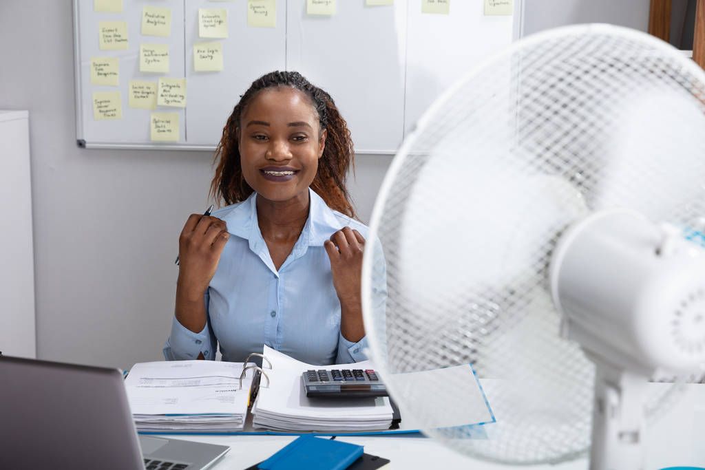Mladá podnikatelka sedí v kanceláři a užívá si vánek s elektrickým ventilátorem - Fotografie, Obrázek