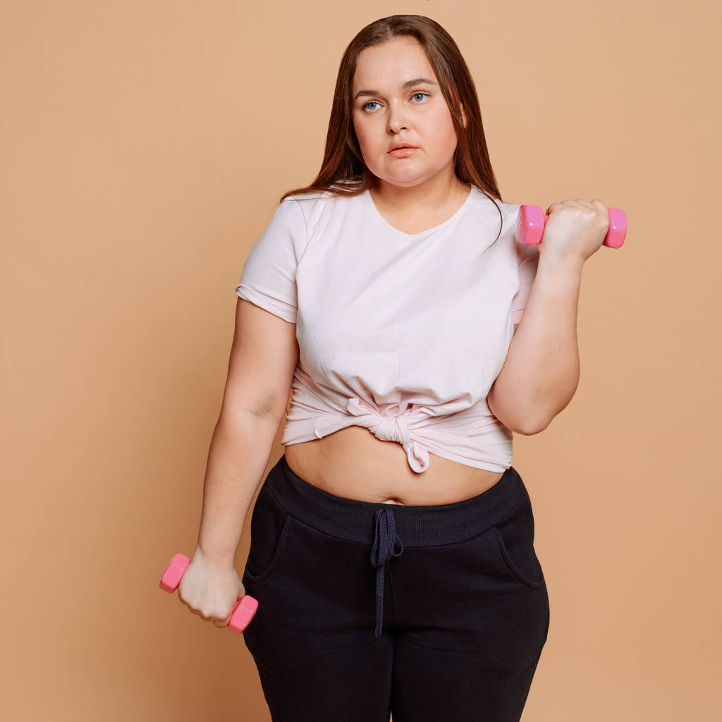 Mujer aburrida con sobrepeso haciendo ejercicio con pesas involuntariamente
 - Foto, imagen