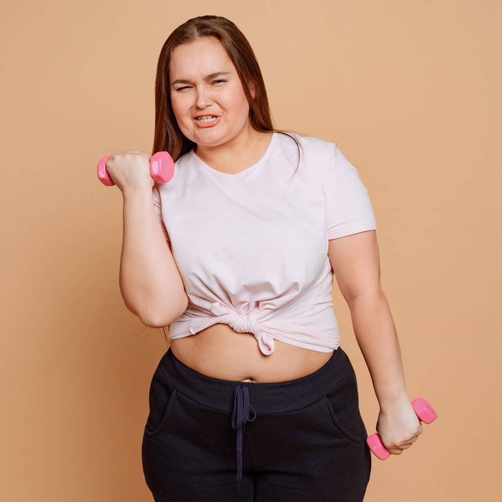 Túlsúlyos lány csinál súlyzó gyakorlatok bézs háttér - Fotó, kép