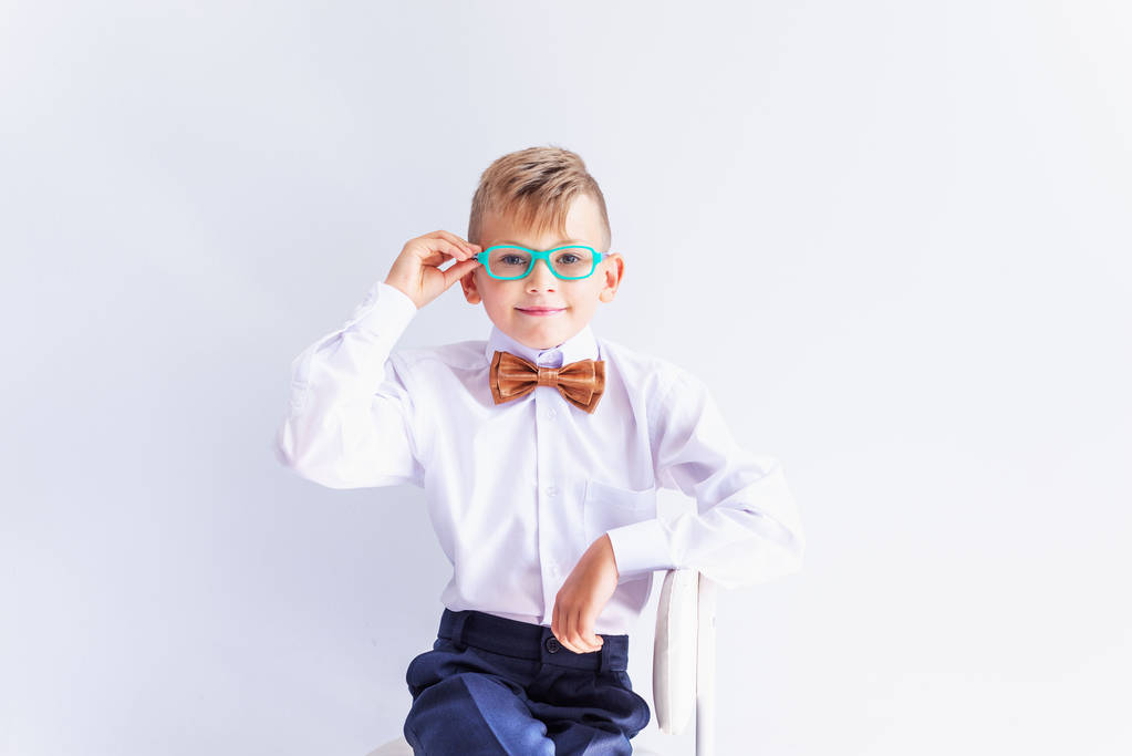 A small cheerful, cute, fashionable blond boy with glasses looks at the camera trying on glass es.The concept of health. Коррекция зрения. Офтальмология
. - Фото, изображение