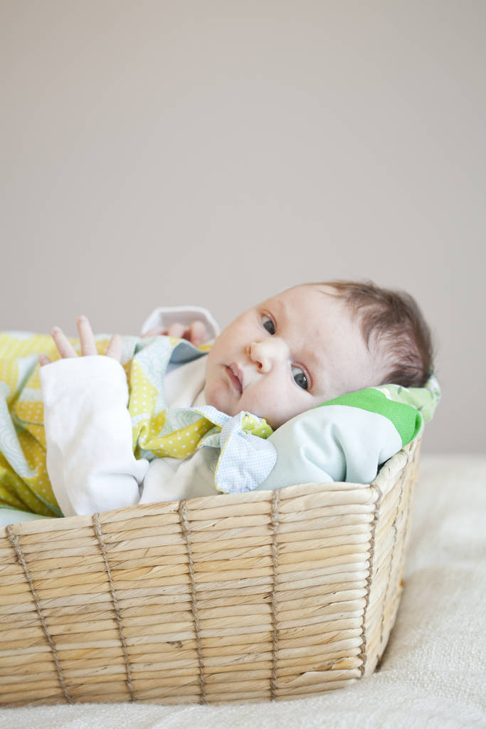 Портрет милой новорожденной девочки, лежащей в корзине, одетой в милое платье
 - Фото, изображение