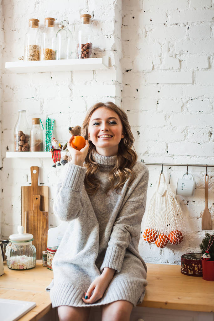 Une fille d'apparence européenne est assise dans la cuisine, jetant ou tenant des agrumes, mandarine, amusant et amusant, la maison et la cuisine
 - Photo, image