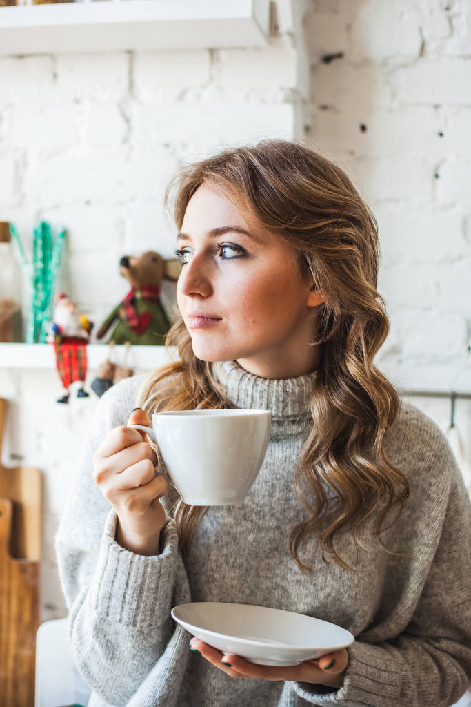 European-looking girl sitting in the kitchen, drinking tea or co - Photo, Image