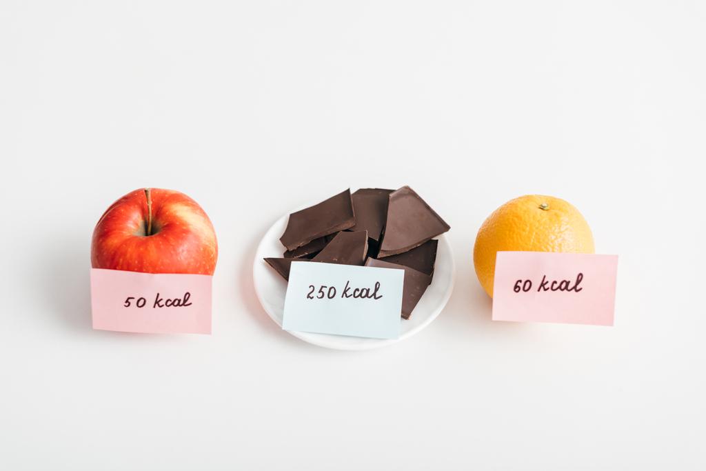 Manzana fresca, naranja y chocolate con calorías en las cartas sobre fondo blanco, dieta de conteo de calorías
 - Foto, Imagen