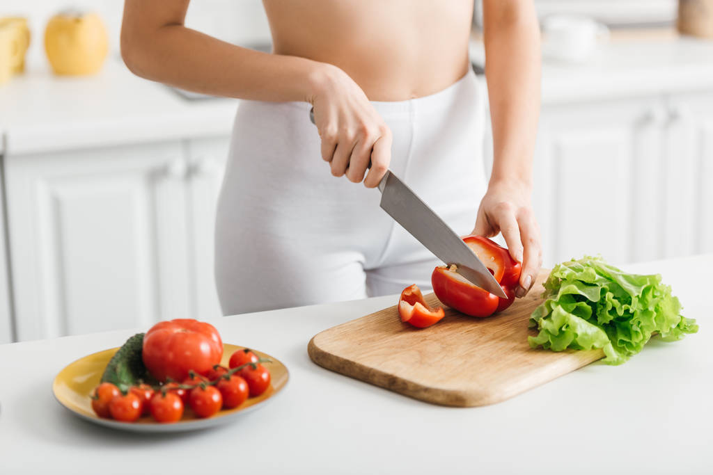 Gesneden weergave van slank meisje snijden rijpe groenten op keukentafel - Foto, afbeelding
