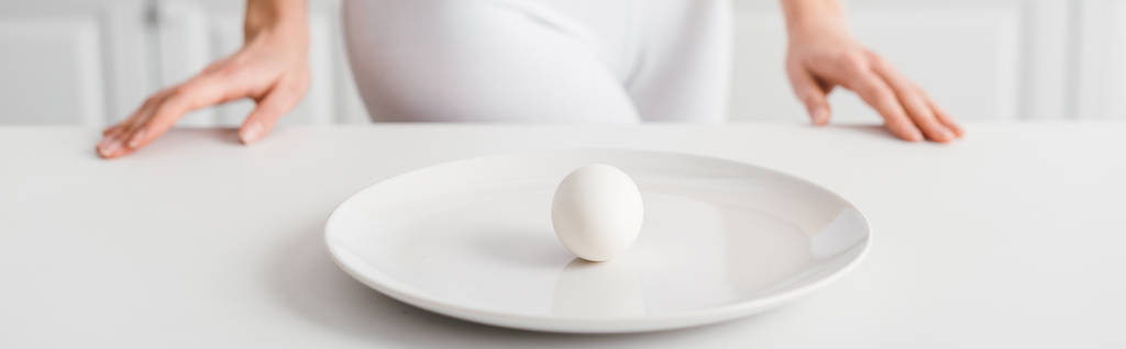 Enfoque selectivo de huevo en plato y niña cerca de la mesa de la cocina, plano panorámico
 - Foto, Imagen