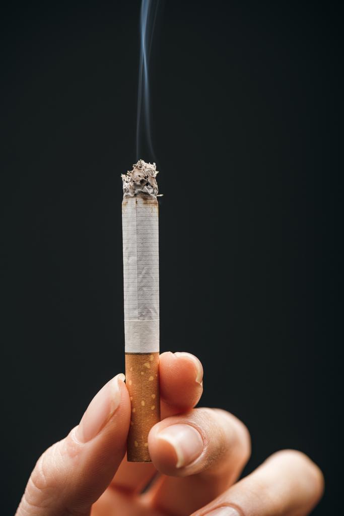 Vista de cerca de la mujer sosteniendo el cigarrillo aislado en negro
  - Foto, imagen