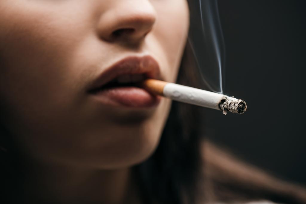 Selective focus of young woman smoking cigarette isolated on black  - Photo, Image