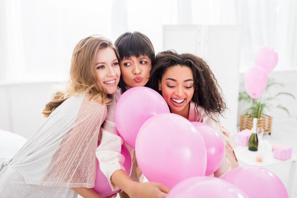 multikulturní emocionální přítelkyně baví s růžovými balónky v ložnici - Fotografie, Obrázek