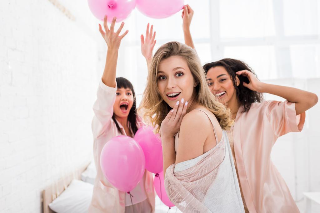 возбужденные мультикультурные девушки веселятся с розовыми шариками на пижамной вечеринке
 - Фото, изображение